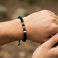 Mano de modelo usando una pulsera tejida en hilo de color negro con esferas lisas 3 oros de 18 quilates con bisutería de calidad de Joyería Caracas. 