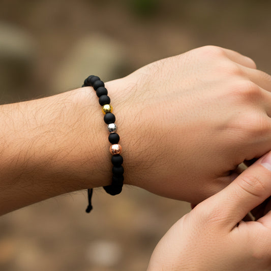 Mano de modelo usando una pulsera tejida en hilo de color negro con esferas lisas 3 oros de 18 quilates con bisutería de calidad de Joyería Caracas. 