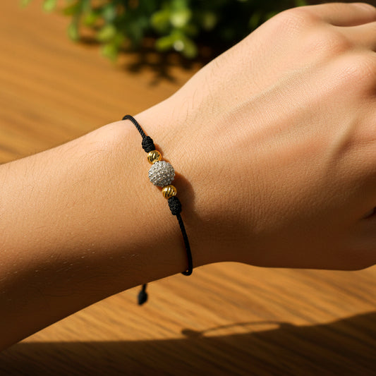 Mano de modelo usando una pulsera tejida de hilo color negro, 2 esferas facetadas en oro amarillo de 18 quilates con bisutería de calidad de Joyería Caracas. 
