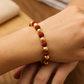 Mano de mujer usando una pulsera tejida con bisutería de color rojo y esferas facetadas en oro amarillo de 18 quilates de Joyería Caracas. 