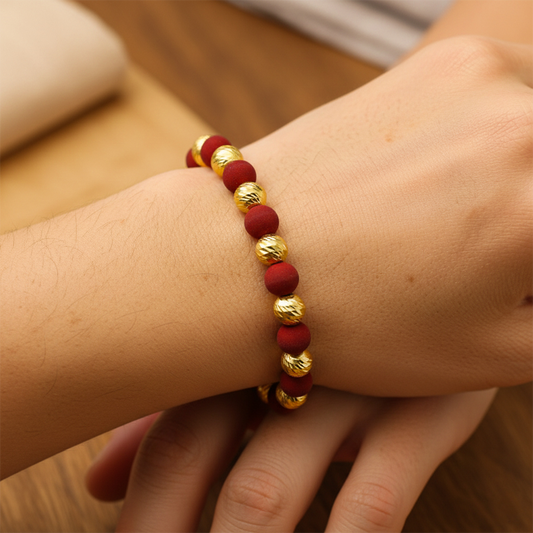 Mano de mujer usando una pulsera tejida con bisutería de color rojo y esferas facetadas en oro amarillo de 18 quilates de Joyería Caracas. 