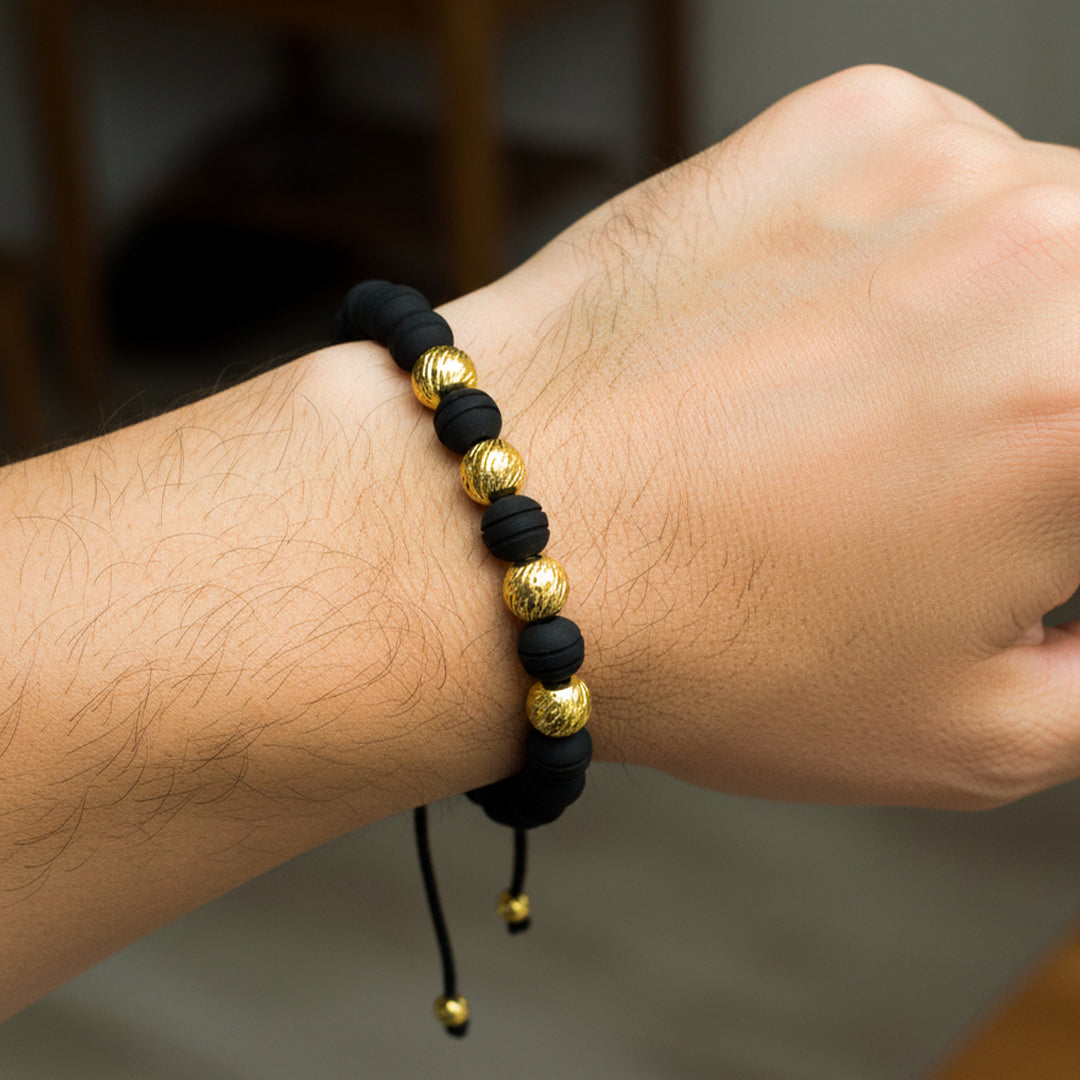 Mano de modelo usando una pulsera tejida en hilo de color negro con esferas facetadas en oro amarillo de 18 quilates con bisutería de calidad de Joyería Caracas. 