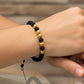 Mano de modelo usando una pulsera tejida en hilo color negro con esferas facetadas en oro amarillo de 18 quilates con bisutería de calidad de Joyería Caracas. 