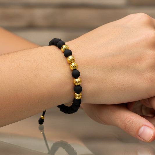 Mano de modelo usando una pulsera tejida en hilo color negro con esferas facetadas en oro amarillo de 18 quilates con bisutería de calidad de Joyería Caracas. 