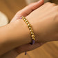Mano de mujer usando una pulsera tejida de hilo color lila con esferas facetadas y lisas en oro amarillo de 18 quilates de Joyería Caracas. 
