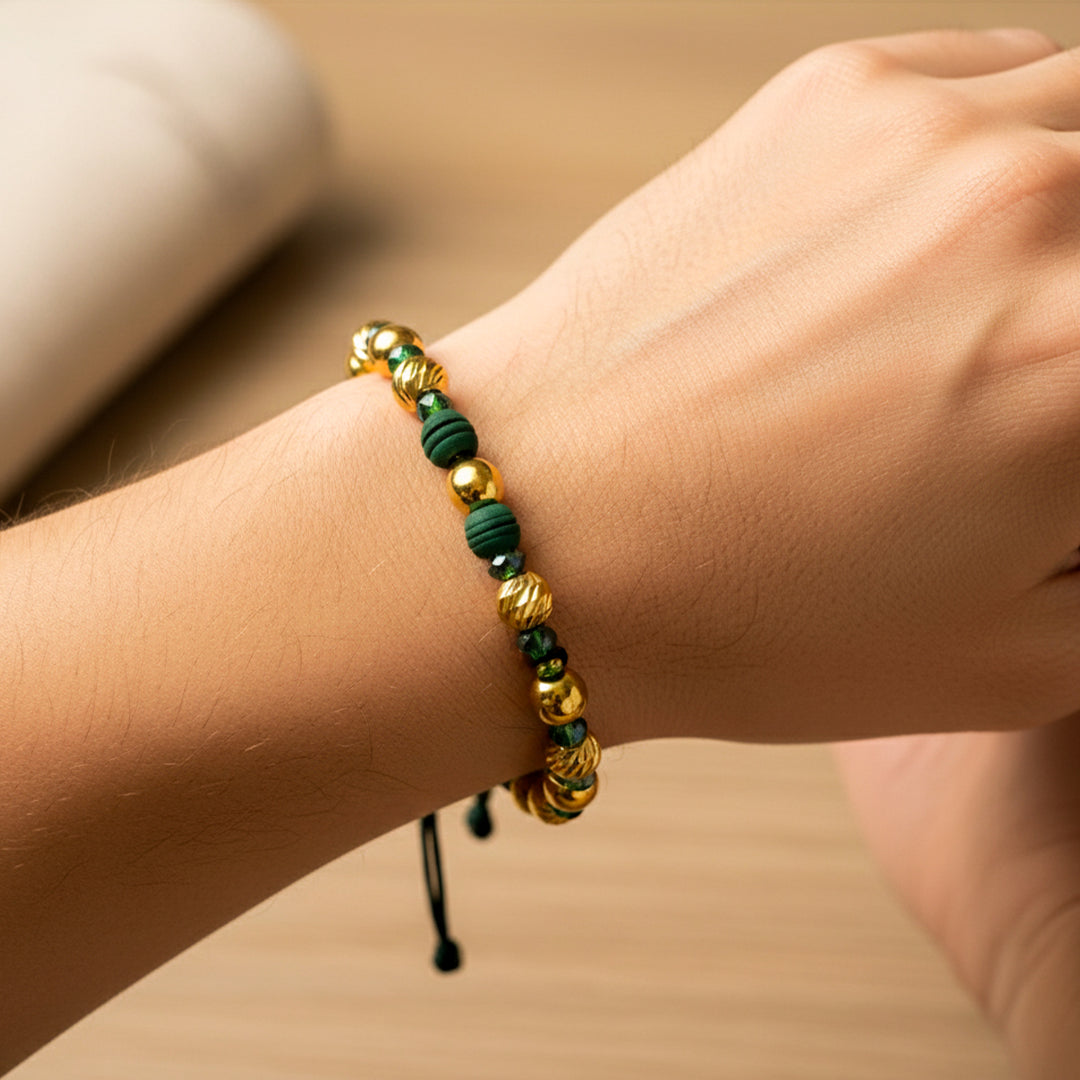 Mano de modelo usando una pulsera tejida en hilo color verde con esferas lisas y facetadas en oro amarillo de 18 quilates con bisutería de calidad de Joyería Caracas. 