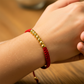 Mano de modelo usando una pulsera tejida en hilo color rojo con esferas facetadas en oro amarillo de 18 quilates de Joyería Caracas. 