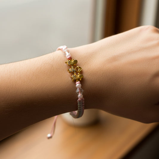 Mano de modelo usando una pulsera tejida en hilo color rosa con dije de familia en oro amarillo de 18 quilates de Joyería Caracas. 