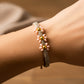 Mano de mujer usando una pulsera tejida en hilo color marrón claro con 3 esferas lisas en oro amarillo de 18 quilates con bisutería de calidad de Joyería Caracas. 