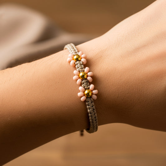 Mano de mujer usando una pulsera tejida en hilo color marrón claro con 3 esferas lisas en oro amarillo de 18 quilates con bisutería de calidad de Joyería Caracas. 