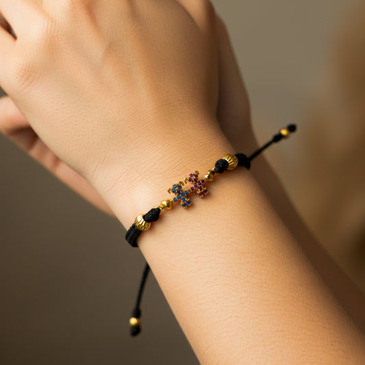 Mano de mujer usando una pulsera tejida en hilo de color negro con herraje de forma de niñas, corazones y 2 esferas facetadas en oro amarillo de 18 quilates de Joyería Caracas. 