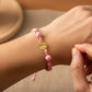 Mano de modelo usando una pulsera tejida en hilo de color rosa con dije de la Virgen de Guadalupe en oro amarillo de 18 quilates de Joyería Caracas. 