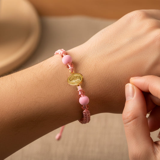 Mano de modelo usando una pulsera tejida en hilo de color rosa con dije de la Virgen de Guadalupe en oro amarillo de 18 quilates de Joyería Caracas. 