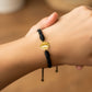 Mano de modelo usando una pulsera tejida en hilo color negro con dije de la Virgen de Guadalupe en oro amarillo de 18 quilates de Joyería Caracas. 