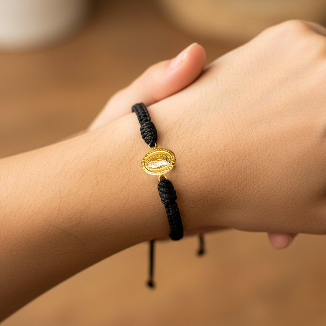 Mano de modelo usando una pulsera tejida en hilo color negro con dije de la Virgen de Guadalupe en oro amarillo de 18 quilates de Joyería Caracas. 