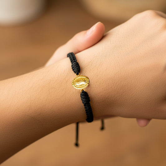 Mano de modelo usando una pulsera tejida en hilo color negro con dije de la Virgen de Guadalupe en oro amarillo de 18 quilates de Joyería Caracas. 