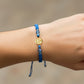 Mano de modelo usando una pulsera tejida en hilo color celeste con dije de la Virgen de Guadalupe en oro amarillo de 18 quilates de Joyería Caracas. 