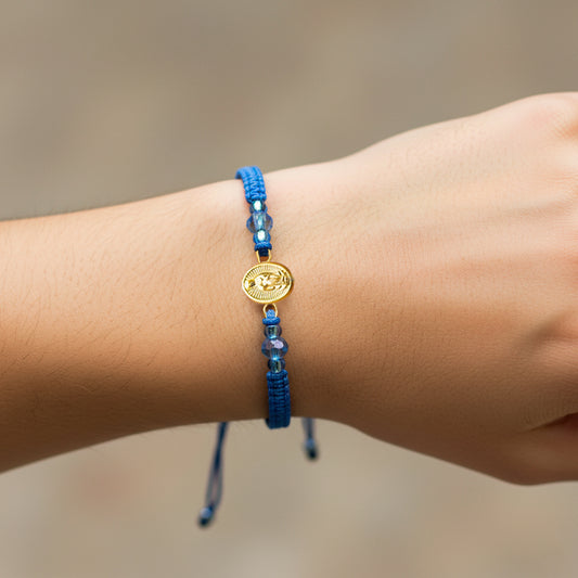 Mano de modelo usando una pulsera tejida en hilo color celeste con dije de la Virgen de Guadalupe en oro amarillo de 18 quilates de Joyería Caracas. 