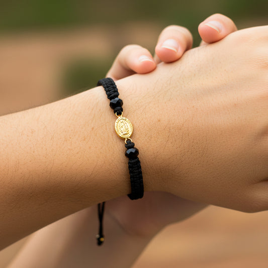 Mano de modelo usando una pulsera tejida en hilo color negro con dije de la Virgen de Guadalupe en oro amarillo de 18 quilates de Joyería Caracas. 