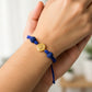 Mano de modelo usando una pulsera tejida en hilo color azul oscuro con dije de la Virgen de Guadalupe en oro amarillo de 18 quilates y bisutería de calidad de Joyería Caracas.
