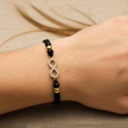 Mano modelo usando una pulsera tejida en hilo color negro con dije en forma de infinito con esferas lisas en oro amarillo de 18 quilates con cristales de color blanco y bisutería de calidad de Joyería Caracas. 
