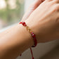 Mano de modelo usando una pulsera tejida en hilo color rojo, herraje en forma de infinito en oro amarillo de 18 quilates con bisutería de calidad de Joyería Caracas. 