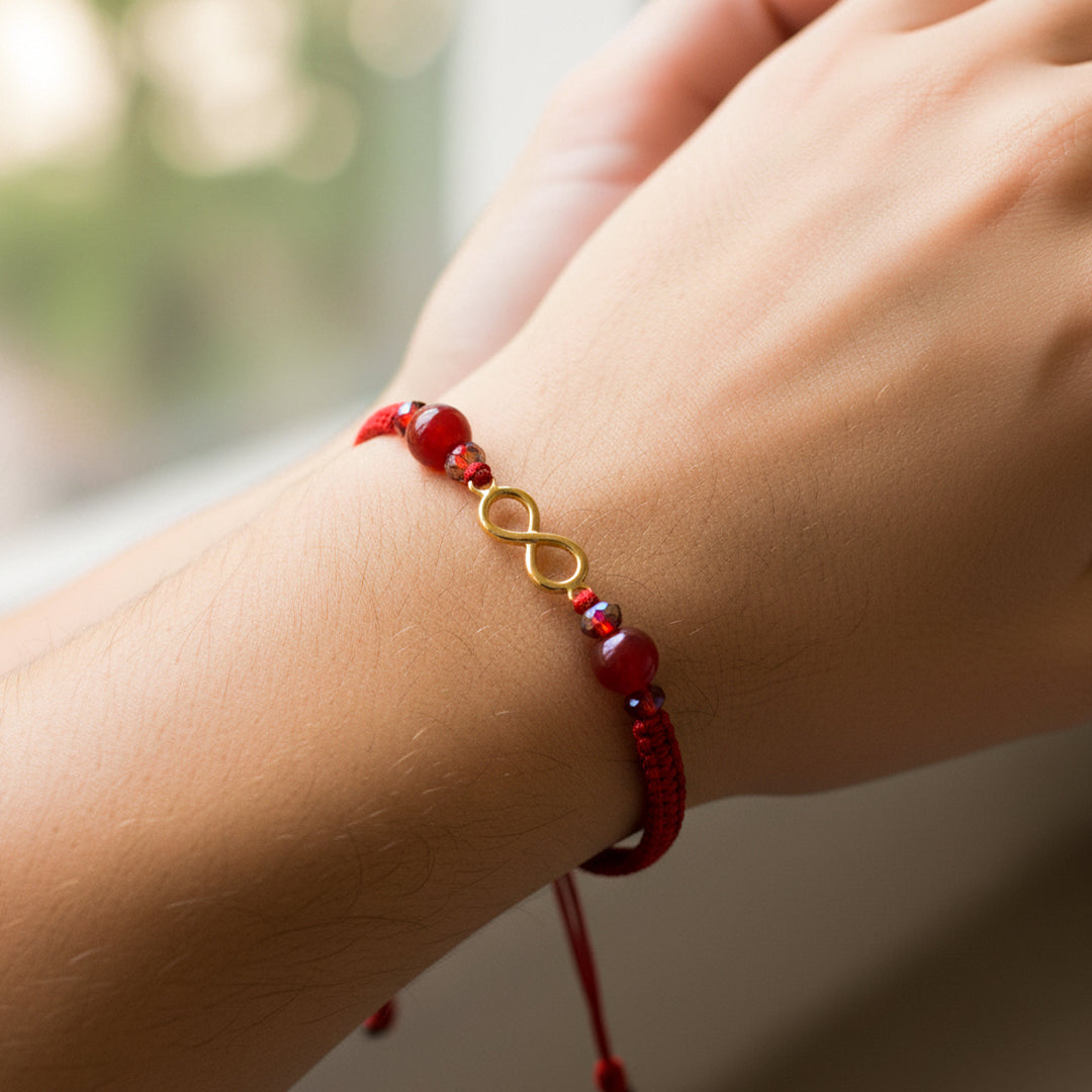 Mano de modelo usando una pulsera tejida en hilo color rojo, herraje en forma de infinito en oro amarillo de 18 quilates con bisutería de calidad de Joyería Caracas. 