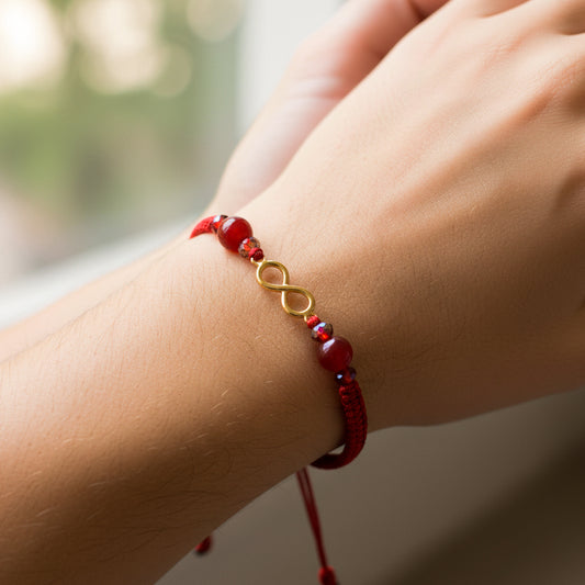Mano de modelo usando una pulsera tejida en hilo color rojo, herraje en forma de infinito en oro amarillo de 18 quilates con bisutería de calidad de Joyería Caracas. 
