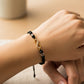 Mano de modelo usando una pulsera tejida en hilo color negro con dije de infinito en oro amarillo de 18 quilates con bisutería de calidad de Joyería Caracas.
