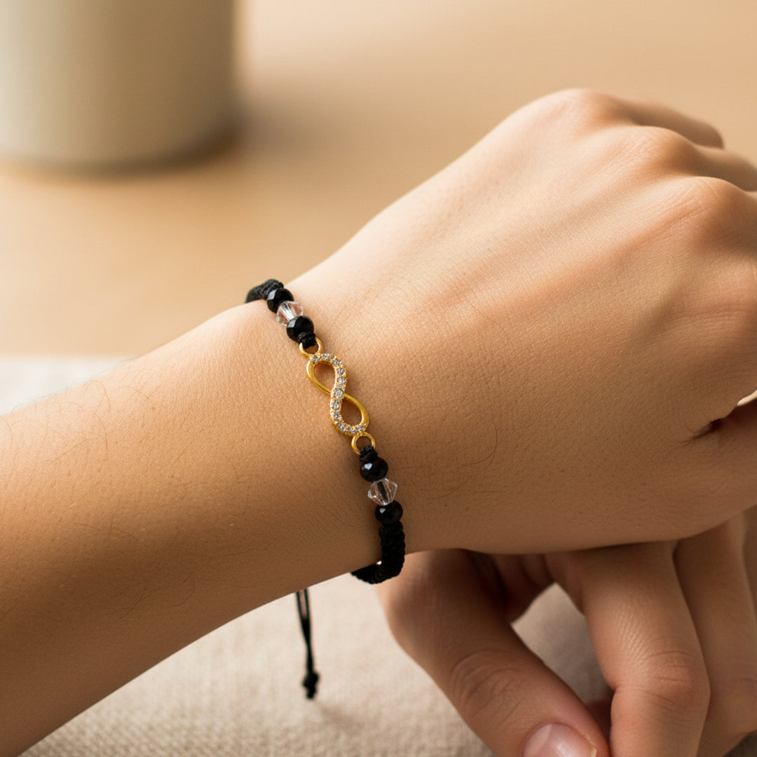 Mano de modelo usando una pulsera tejida en hilo color negro con dije de infinito en oro amarillo de 18 quilates con bisutería de calidad de Joyería Caracas.