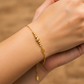 Mano de mujer usando una pulsera con esferas lisas, facetadas y un dije en forma de hoja en oro amarillo de 18 quilates de Joyería Caracas. 