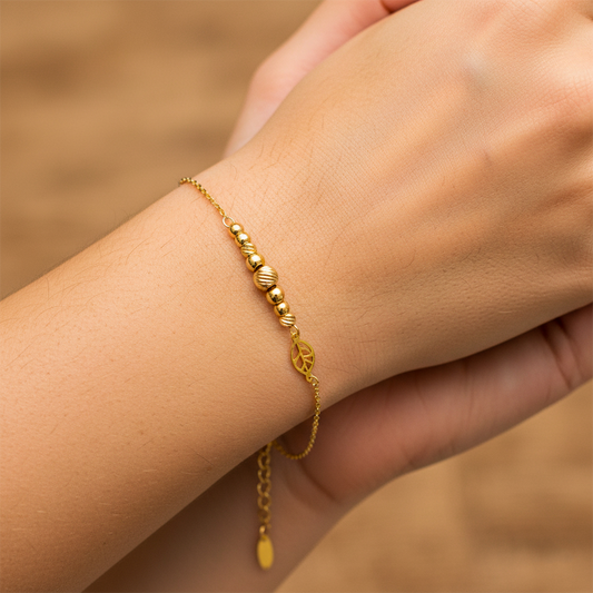 Mano de mujer usando una pulsera con esferas lisas, facetadas y un dije en forma de hoja en oro amarillo de 18 quilates de Joyería Caracas. 