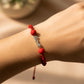 Mano de modelo usando una pulsera tejida en hilo de color rojo con un dije de la palabra love en oro blanco de 18 quilates con cristales de color blanco y bisutería de calidad de Joyería Caracas. 