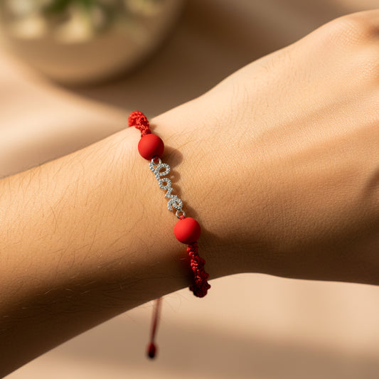 Mano de modelo usando una pulsera tejida en hilo de color rojo con un dije de la palabra love en oro blanco de 18 quilates con cristales de color blanco y bisutería de calidad de Joyería Caracas. 