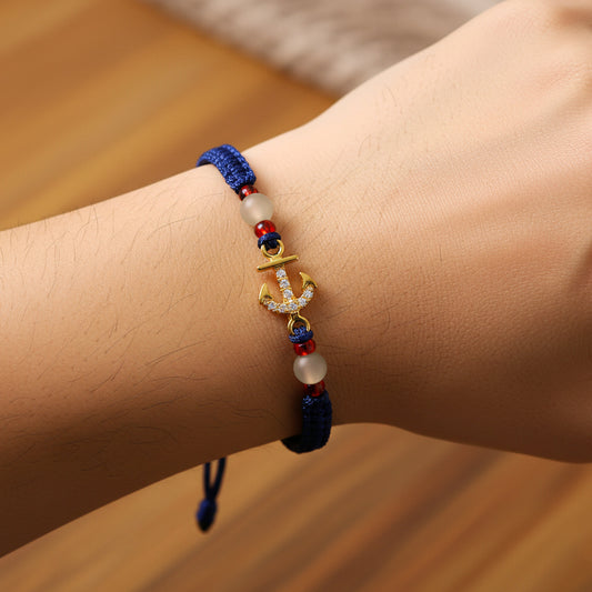 Mano de modelo usando una pulsera tejida en hilo color azul oscuro, con dije de ancla en oro amarillo de 18 quilates con cristales de color blanco y bisutería de calidad de Joyería Caracas. 
