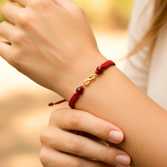 Mano de modelo usando una pulsera tejida en hilo color rojo con dije de infinito en oro amarillo de 18 quilates con bisutería de calidad de Joyería Caracas. 