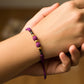 Mano de modelo usando una pulsera tejida en hilo de color morado con esferas lisas en oro amarillo de 18 quilates con bisutería de calidad de Joyería Caracas. 