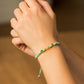 Mano de modelo usando una pulsera tejida de hilo color verde, herraje en forma de osito en oro amarillo de 18 quilates con bisutería de calidad de Joyería Caracas. 