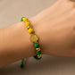 Mano de mujer usando una pulsera tejida personalizada con temática del Atlético Bucaramanga con placa grabada del AB en oro amarillo de 18 quilates de Joyería Caracas. 