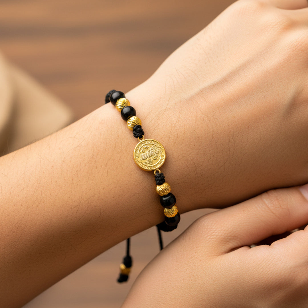 Mano de modelo usando una pulsera tejida en hilo de color negro con dije de San Benito y esferas facetadas en oro amarillo de 18 quilates de Joyería Caracas.
