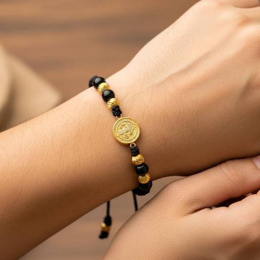 Mano de modelo usando una pulsera tejida en hilo de color negro con dije de San Benito y esferas facetadas en oro amarillo de 18 quilates de Joyería Caracas.