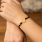 Mano de modelo usando una pulsera tejida en hilo color negro con dije San Benito y esferas lisas en oro amarillo de 18 quilates de Joyería Caracas. 