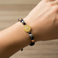 Mano de modelo usando una pulsera tejida en hilo color negro con dije de San Benito y esferas lisas en 3 oros de 18 quilates de Joyería Caracas. 