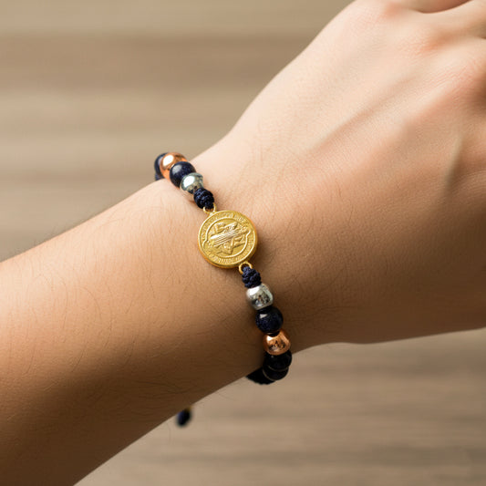 Mano de modelo usando una pulsera tejida en hilo color negro con dije de San Benito y esferas lisas en 3 oros de 18 quilates de Joyería Caracas. 