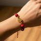 Mano modelo usando una pulsera tejida en hilo color rojo con dije San Benito y esferas lisas en oro amarillo de 18 quilates con bisutería de calidad de Joyería Caracas. 