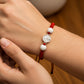 Mano de modelo usando una pulsera tejida en hilo de color rojo con dije de San Benito en oro blanco de 18 quilates con bisutería de calidad de Joyería Caracas. 