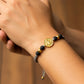 Mano de modelo usando una pulsera tejida con hilo de color gris con dijes de San Benito XL y esferas facetadas en oro amarillo de 18 quilates con bisutería de Joyería Caracas. 