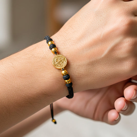 Mano de modelo usando una pulsera tejida en hilo color negro con accesorios, herraje de San Benito con esferas lisas en oro amarillo de 18 quilates de Joyería Caracas. 