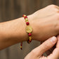 Mano de modelo usando una pulsera tejida en hilo de color rojo, con esferas facetadas y herraje con forma de San Benito en oro amarillo de 18 quilates con bisutería de calidad de Joyería Caracas. 