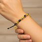 Mano de modelo usando una pulsera tejida en hilo color negro, con dije en forma de San Benito, cruz y esferas lisas en oro amarillo de 18 quilates con bisutería de calidad de Joyería Caracas. 